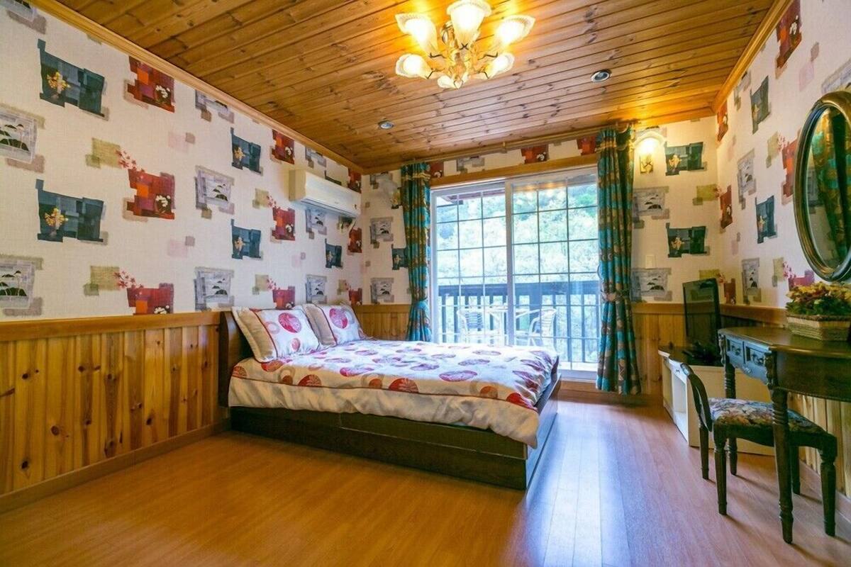 A cozy bedroom with a wooden ceiling, a large bed, a dresser, and a window with curtains.
