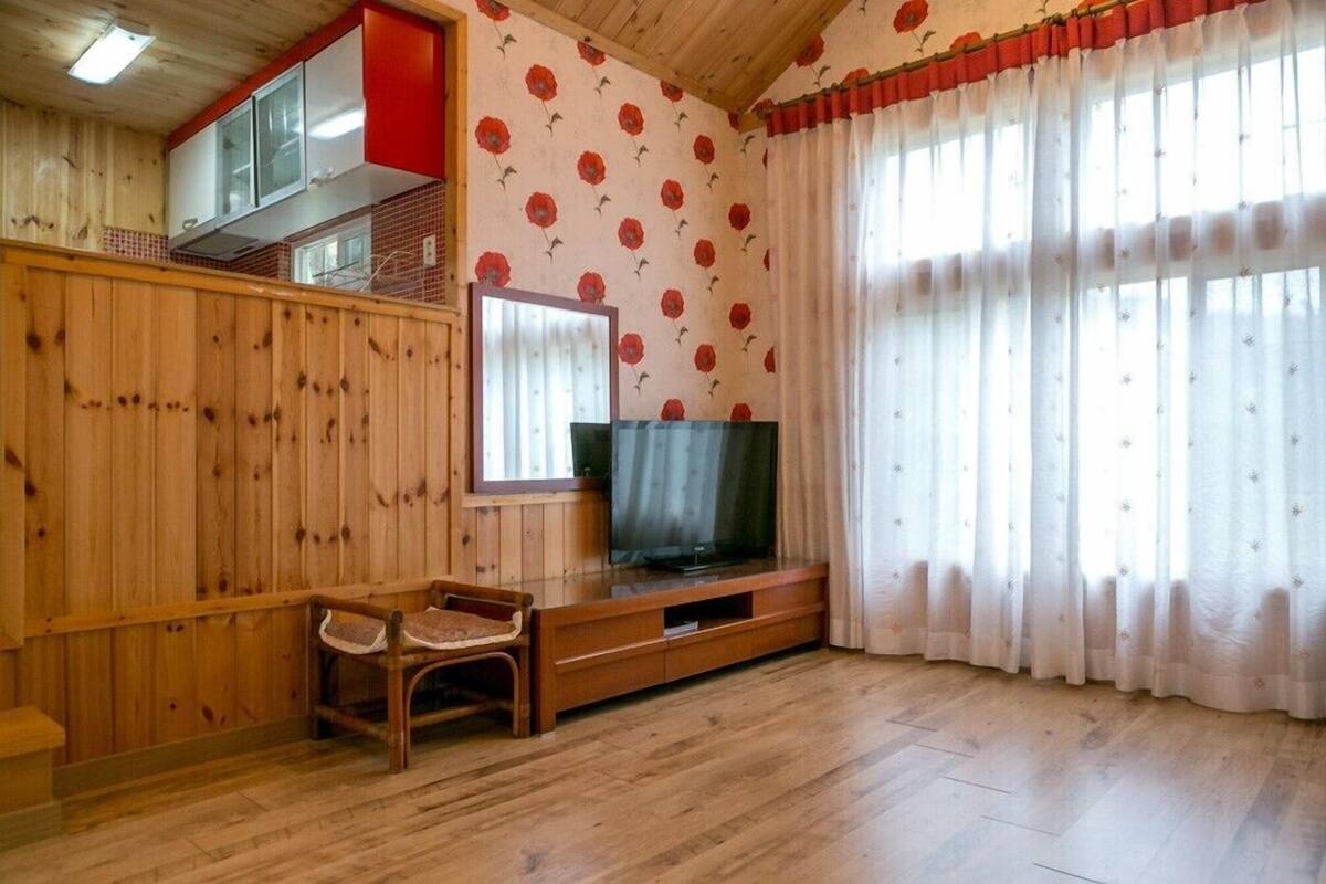 A room with wooden walls, a television on a wooden stand, a chair, and a window with curtains.