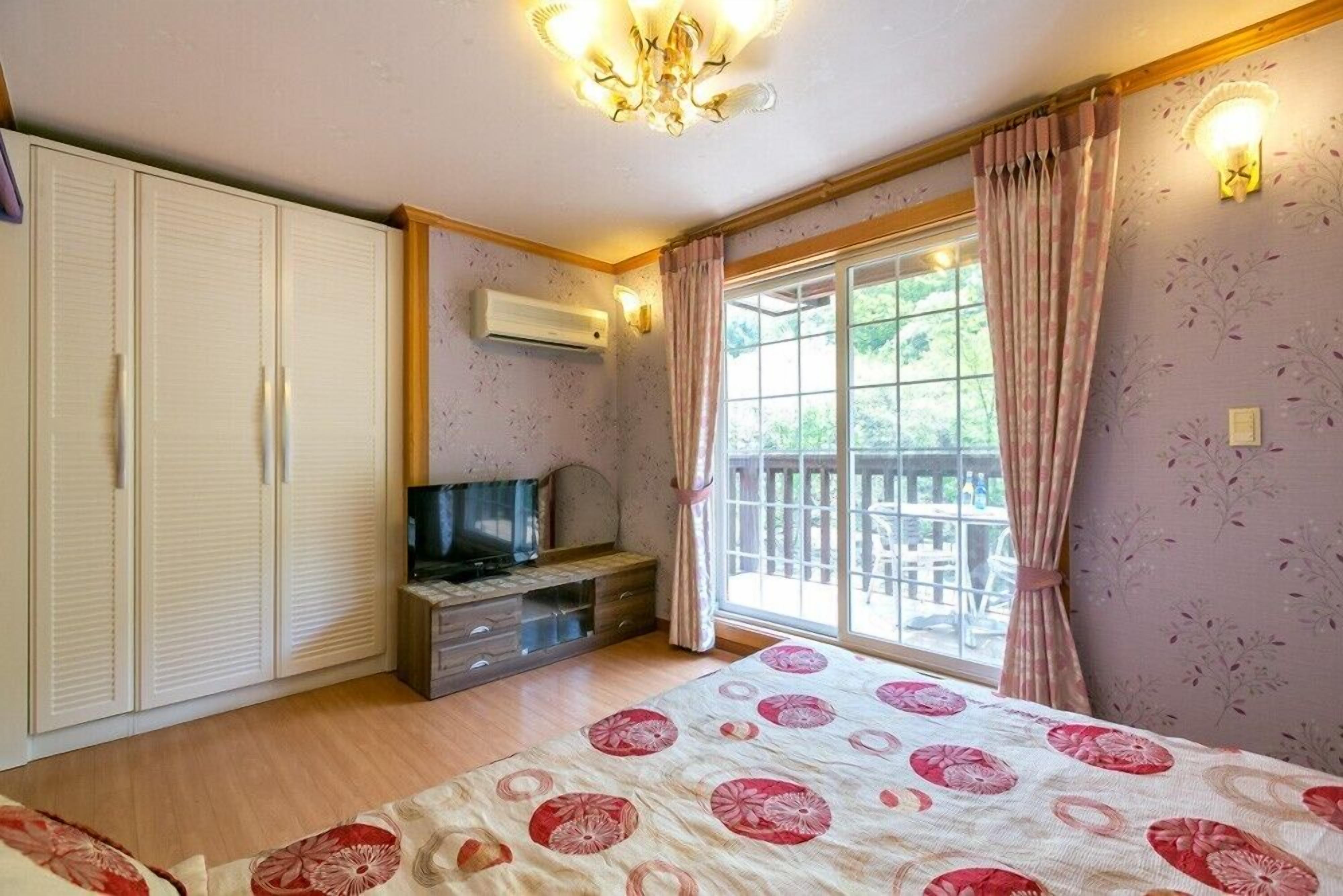 Un dormitorio con cama, televisión, armario y ventana con cortinas.