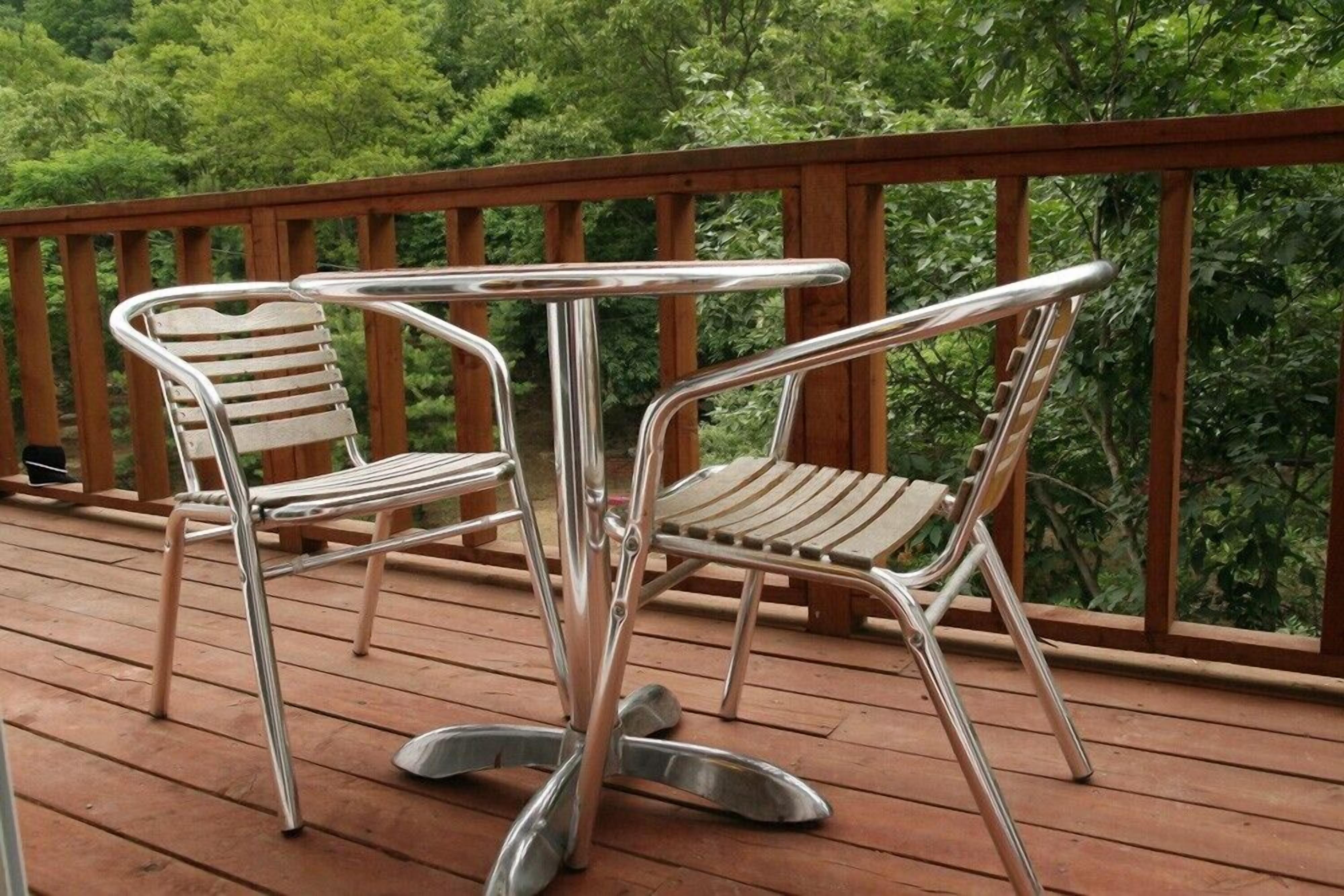 A wooden deck with two metal-framed chairs and a metal table.