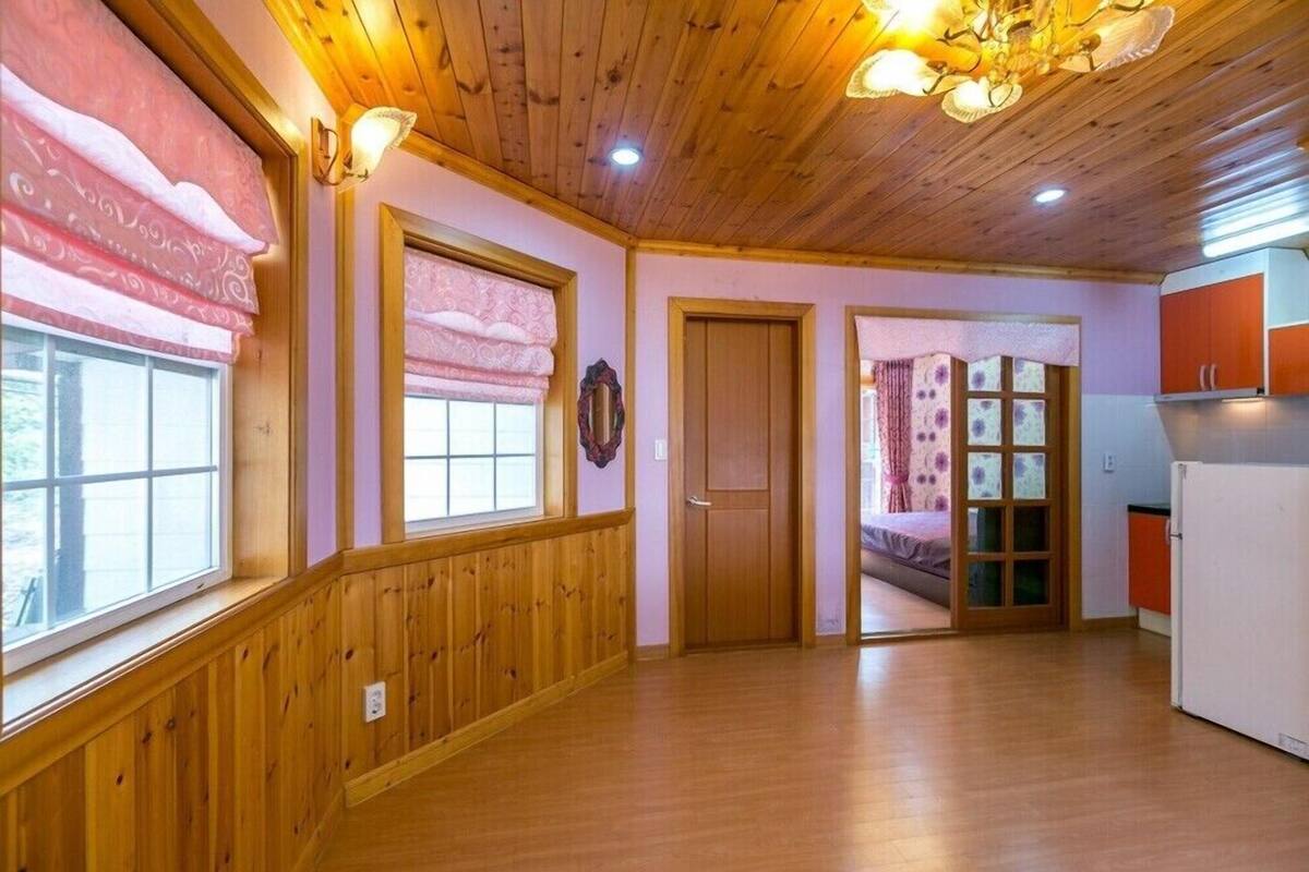 A room with wooden paneling, a wooden ceiling, and a bed with a pink and purple patterned bedspread.