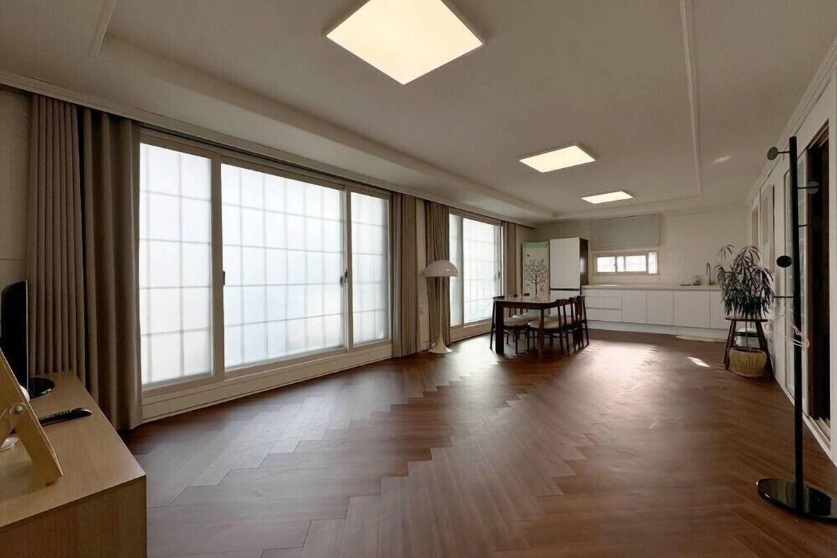 A spacious living area with large windows, a dining table, and a modern ceiling design.