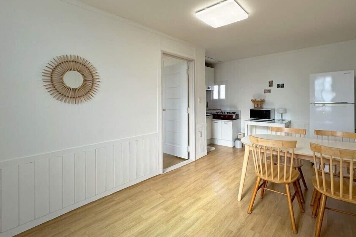 A modern kitchen with white cabinets, a microwave, and a refrigerator. There is a dining area with wooden chairs and a table.