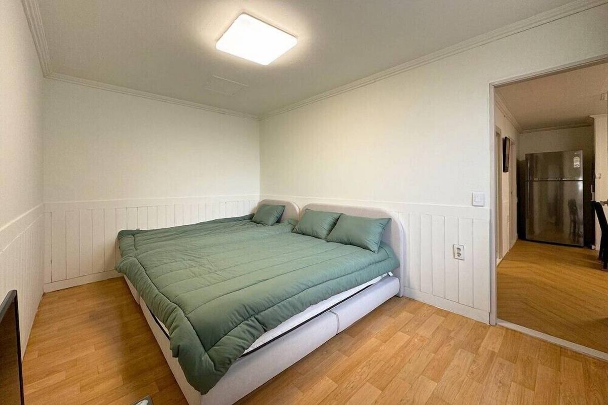 A small, single-bed room with a green bedspread, white walls, and a wooden floor.