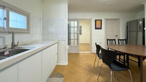 A modern kitchen with white cabinetry, a wooden dining table, and a refrigerator. - Taeyoung Pension (Pohang)