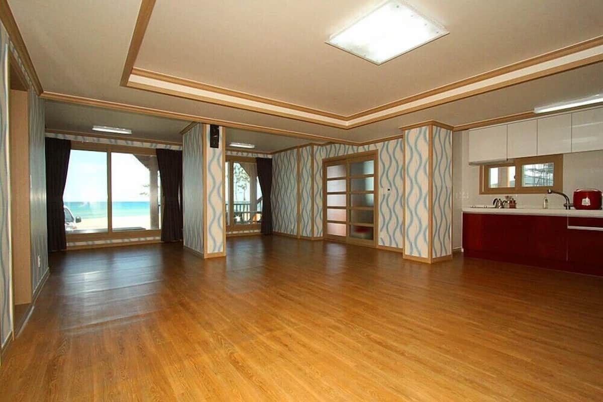 A spacious room with wooden flooring, a kitchen area with white cabinets, and a large sliding glass door leading to a balcony.