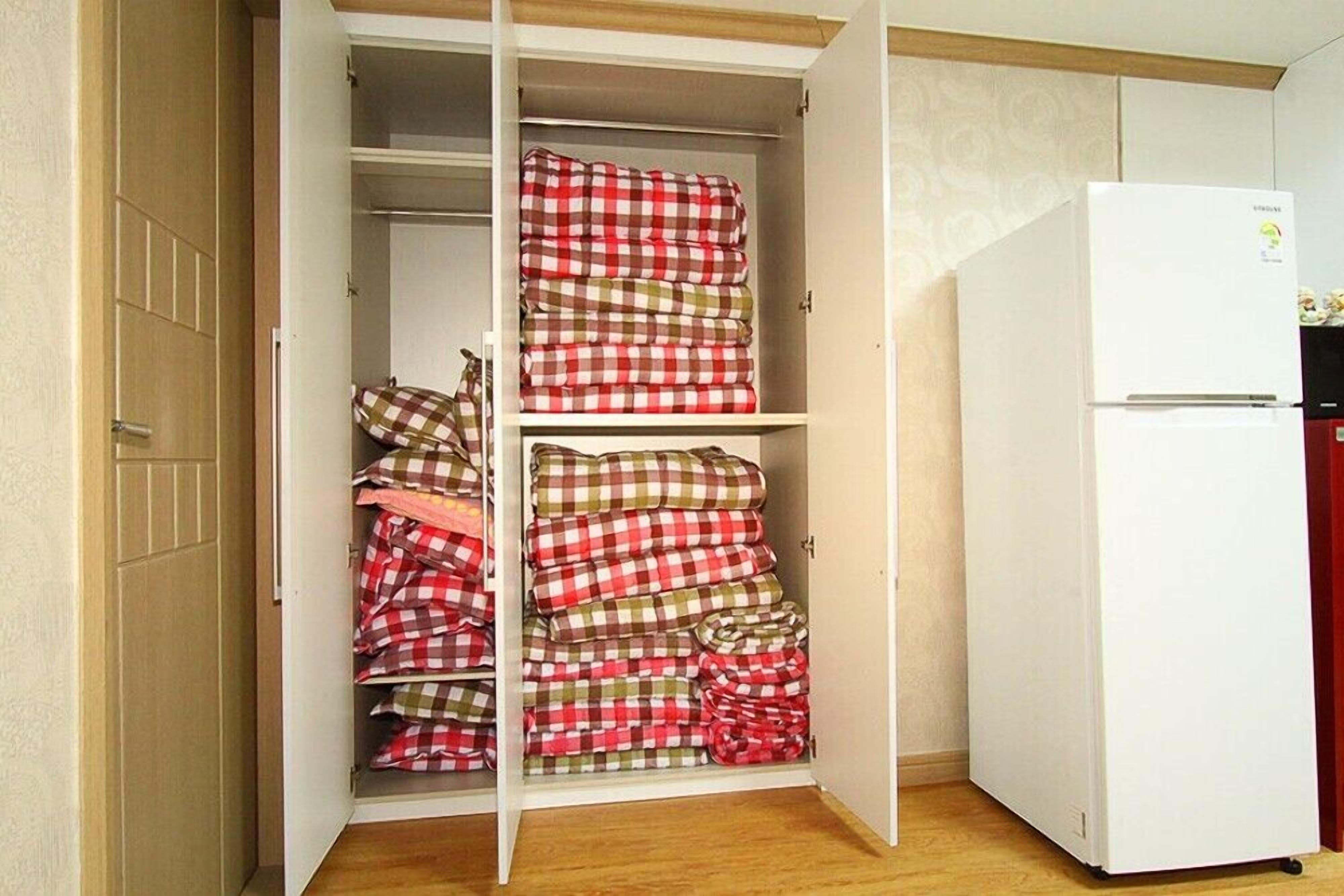 Una habitación con un armario que contiene mantas dobladas y un refrigerador blanco.