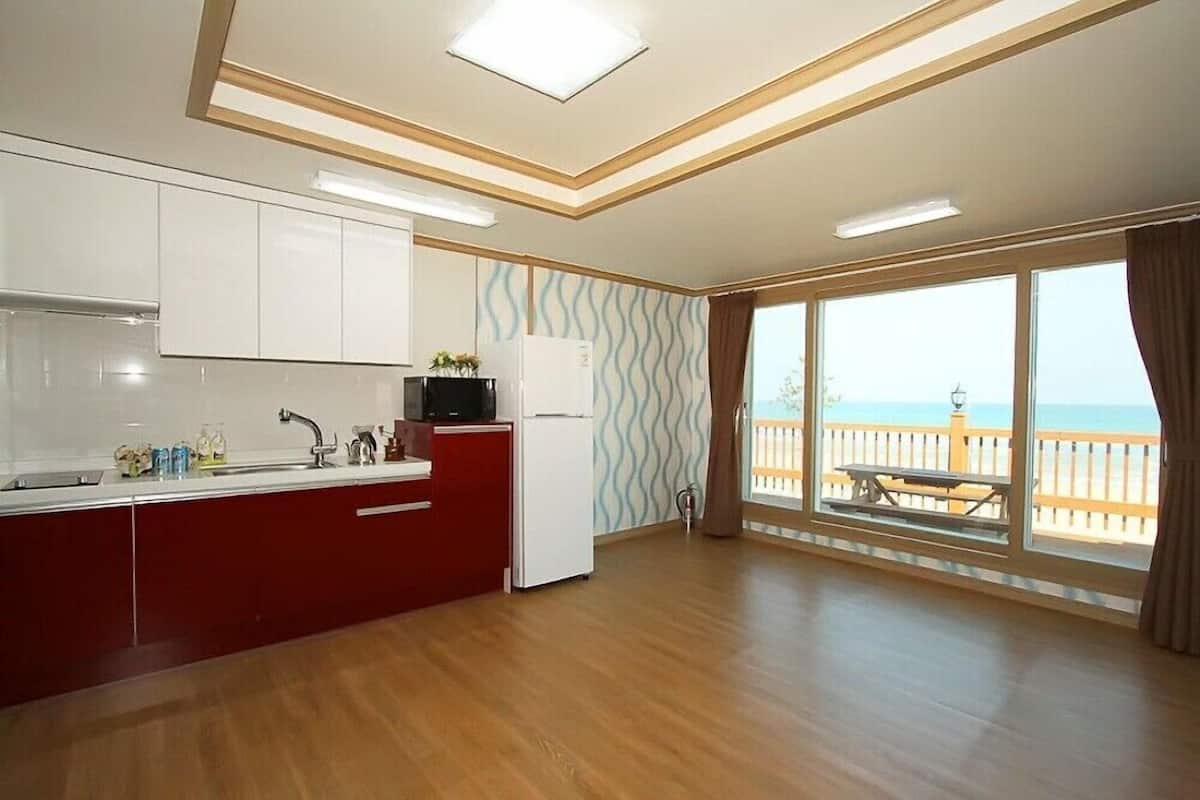 A modern kitchen with white cabinets, a red countertop, and a view of the ocean through large windows.