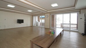 A spacious room with a wooden bench, a television, and large windows. - Wolpo Donghae Pension 2 (Pohang)