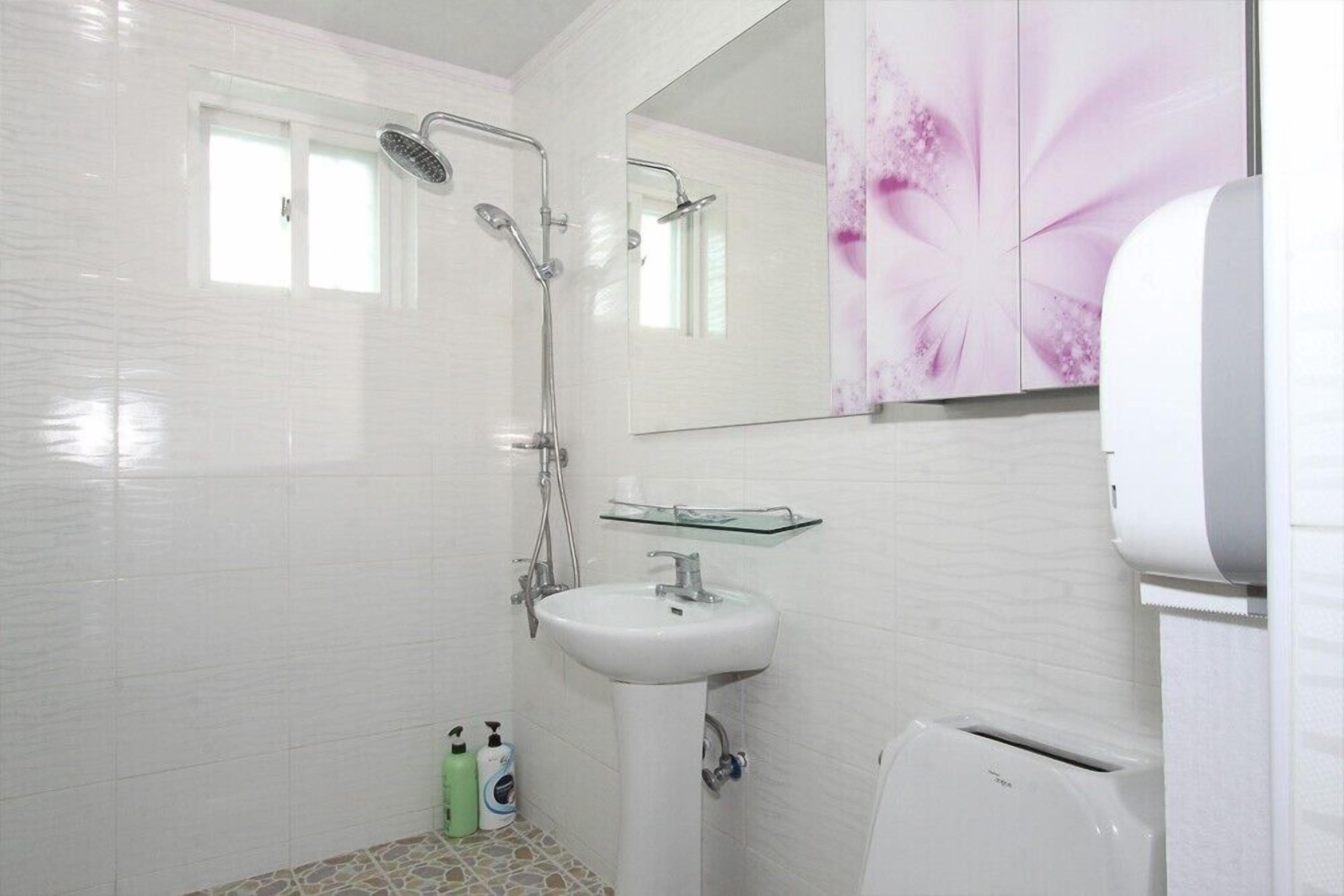 A modern bathroom with white tiles, a glass shower enclosure, a pedestal sink, and a toilet.