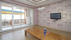 A room with a large sliding glass door leading to an outdoor area, a wooden table, a television mounted on the wall, and patterned wallpaper. - Wolpo Donghae Pension 2 (Pohang)