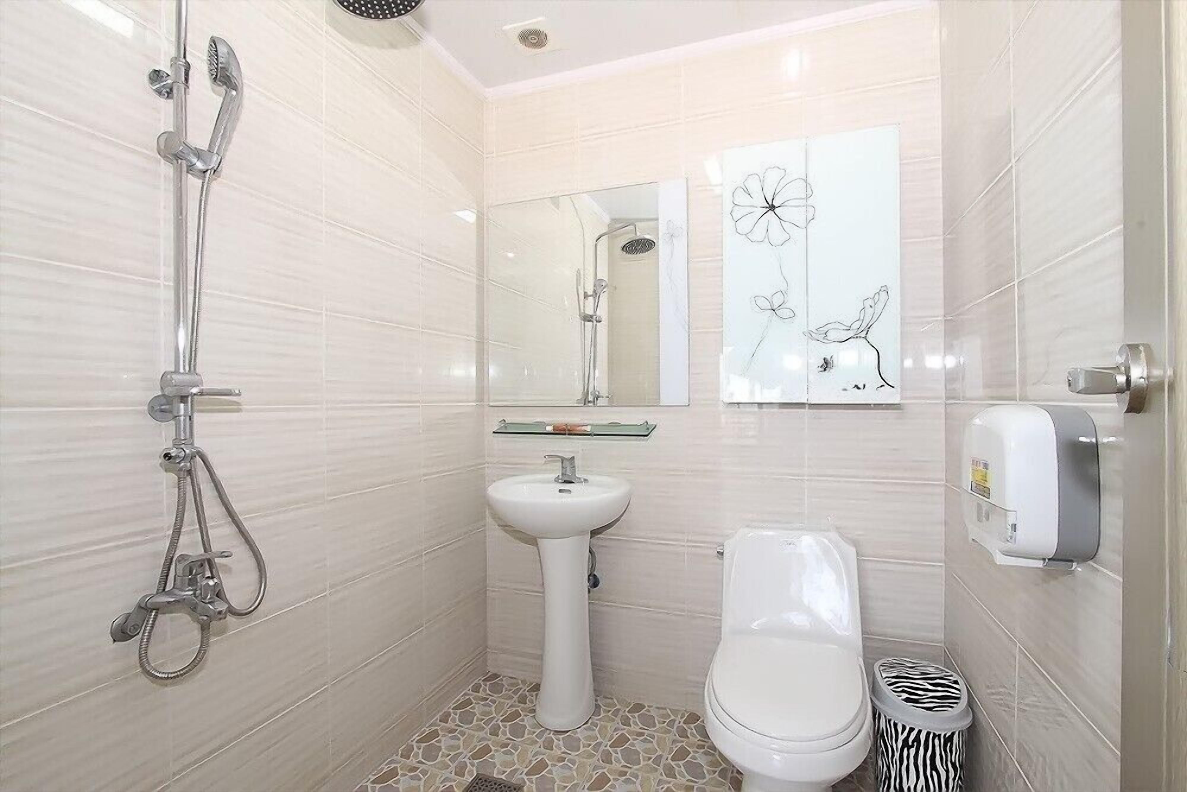 A bathroom with a shower, sink, toilet, and a zebra-patterned trash bin.