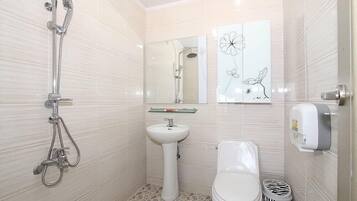 A bathroom with a shower, sink, toilet, and a zebra-patterned trash bin.
