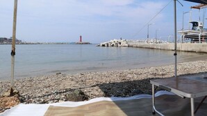 A waterfront view with a pier, a red lighthouse, and a covered seating area. - Damoa Pension (Pohang)