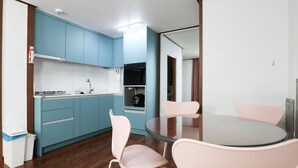 A compact kitchen with blue cabinets, a gas stove, and a small oven. There is a round glass table with four chairs. - Damoa Pension (Pohang)