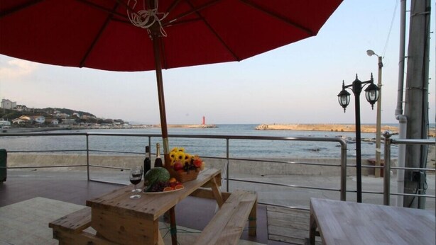 A wooden table with a red umbrella, a bottle, and a basket of fruit. - Damoa Pension (Pohang)