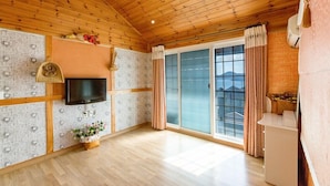 Un'ampia stanza con travi a vista in legno, una TV a schermo piatto montata a parete, una porta vetrata scorrevole che dà su un balcone e un angolo cottura.