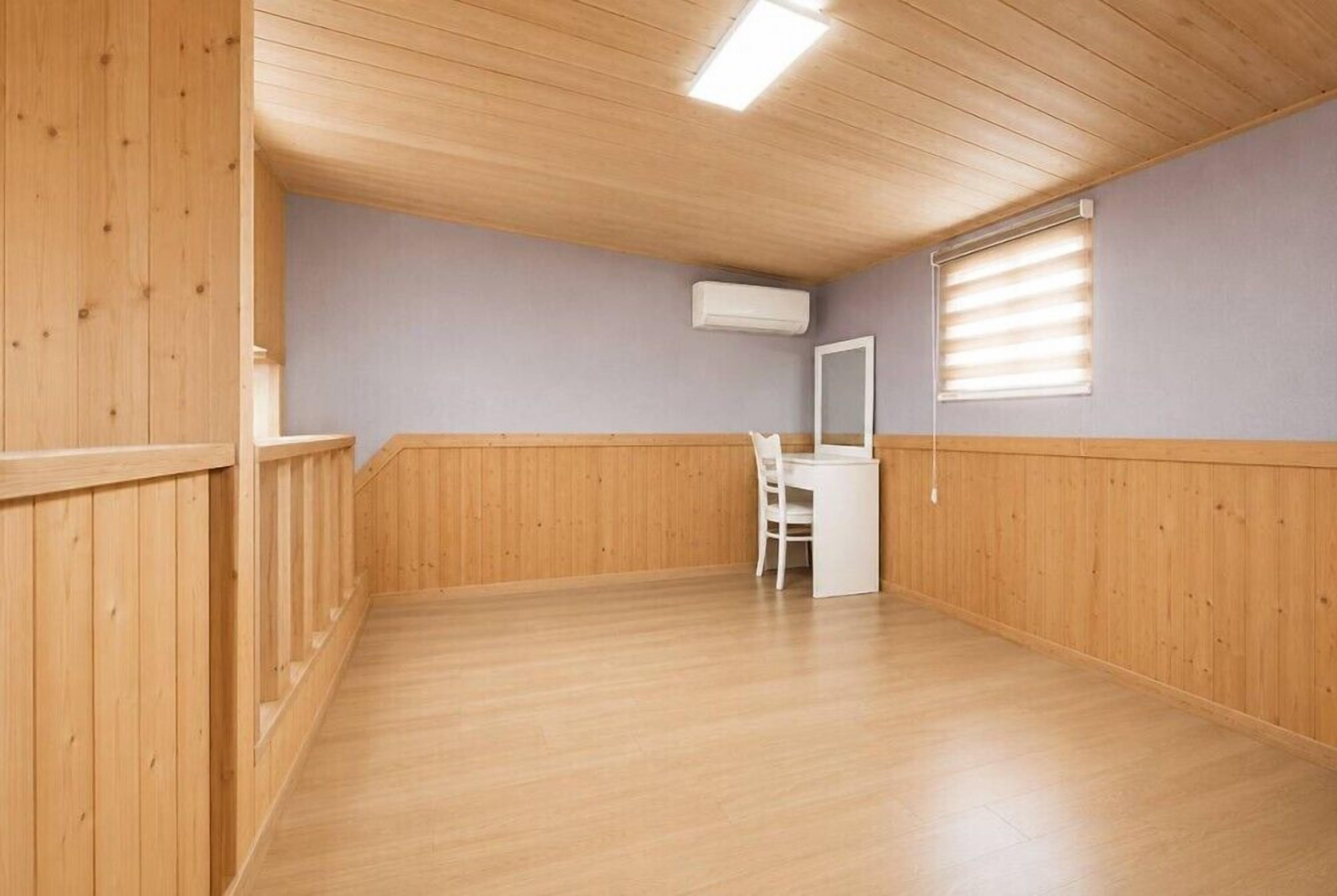 Una habitación con paneles de madera, un escritorio blanco, una silla y una ventana con persianas.