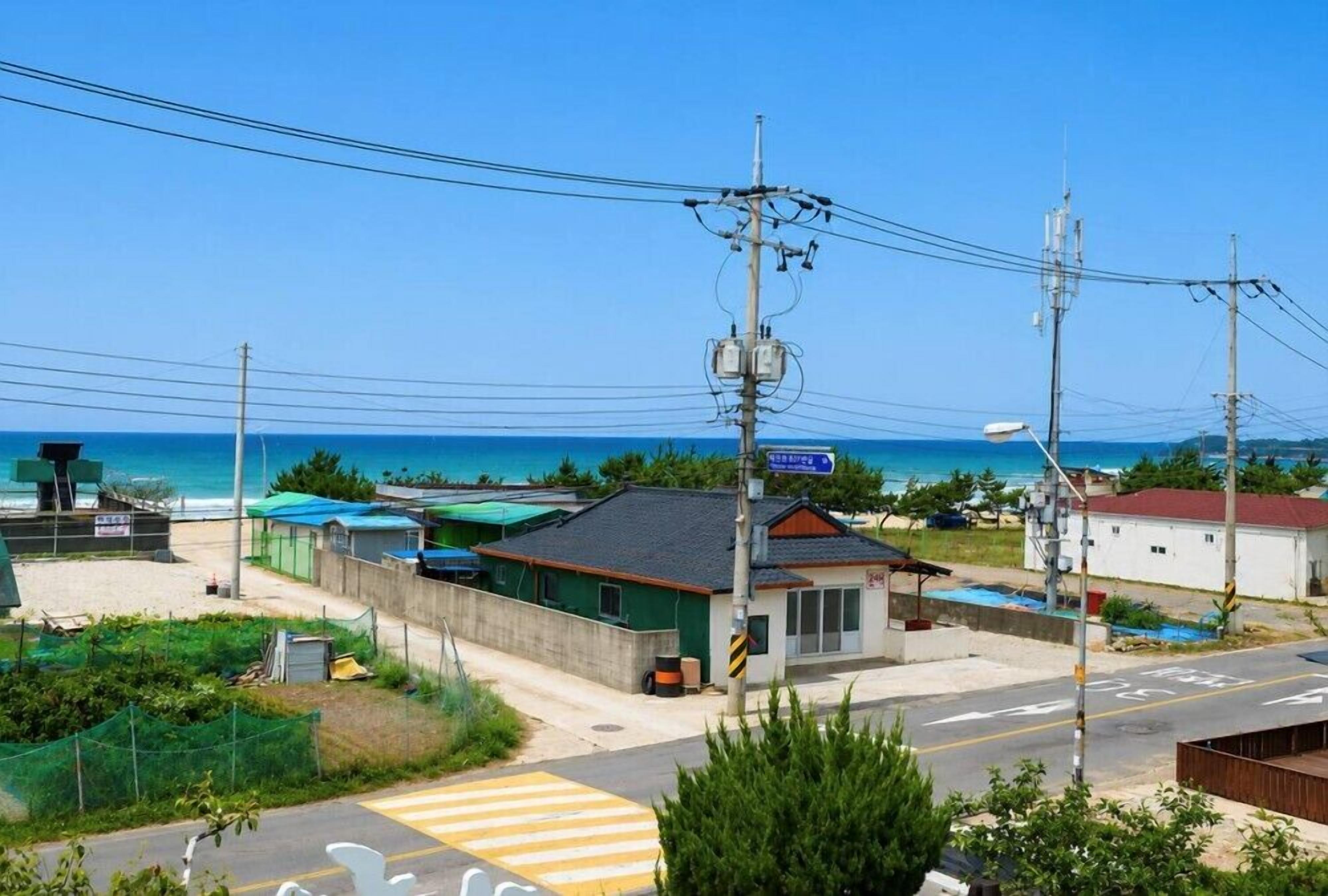 A coastal area with a small building, a road with a pedestrian crossing, and a clear view of the ocean.