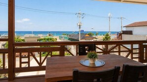 Una terraza de madera con una mesa y sillas, con vistas a una zona costera con edificios y un cielo despejado.