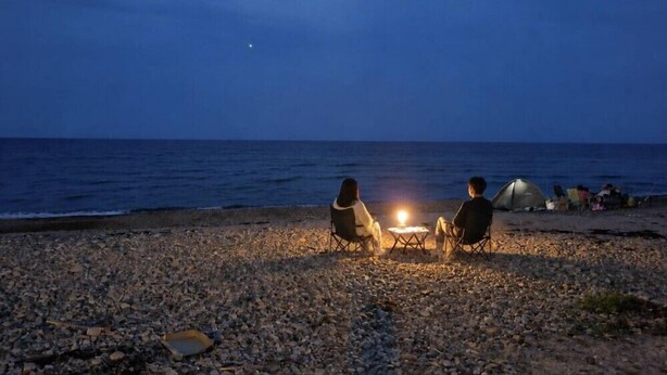 Escena de playa con una fogata, dos sillas y una carpa.