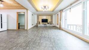 A spacious living room with a large TV, wooden ceiling, and large windows. - Serence Pension (Gapyeong)
