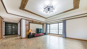 A spacious living room with a wooden floor, a television, and a large window with curtains. - Serence Pension (Gapyeong)