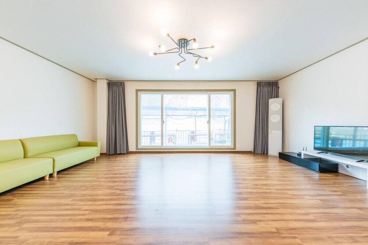 A spacious living room with a green sofa, a flat-screen TV, and a unique ceiling light fixture.