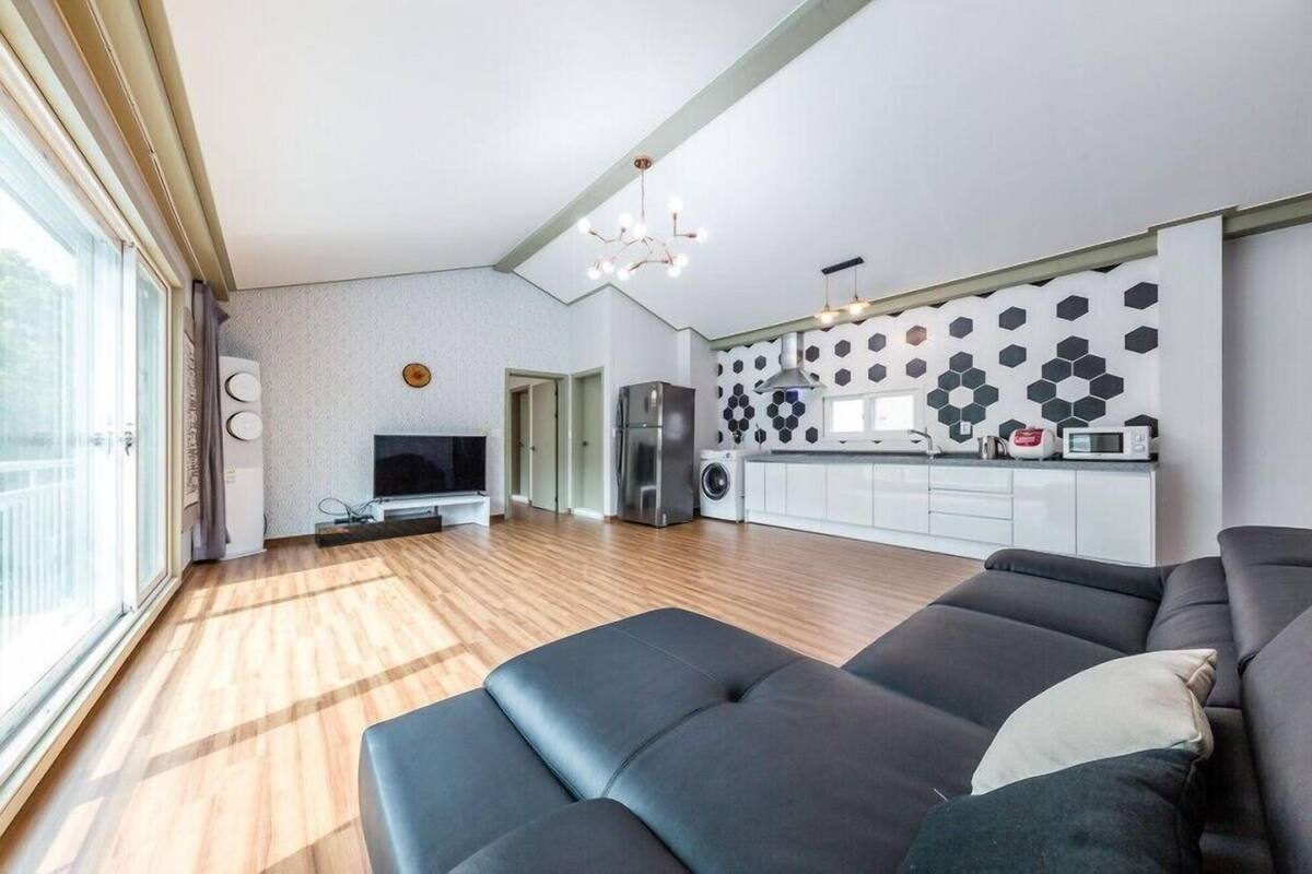 A modern living room with a large black sofa, a flat-screen TV, and a kitchen area with a microwave and refrigerator.