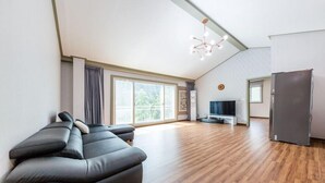 A modern living room with a sectional sofa, a flat-screen TV, and a refrigerator. - Serence Pension (Gapyeong)