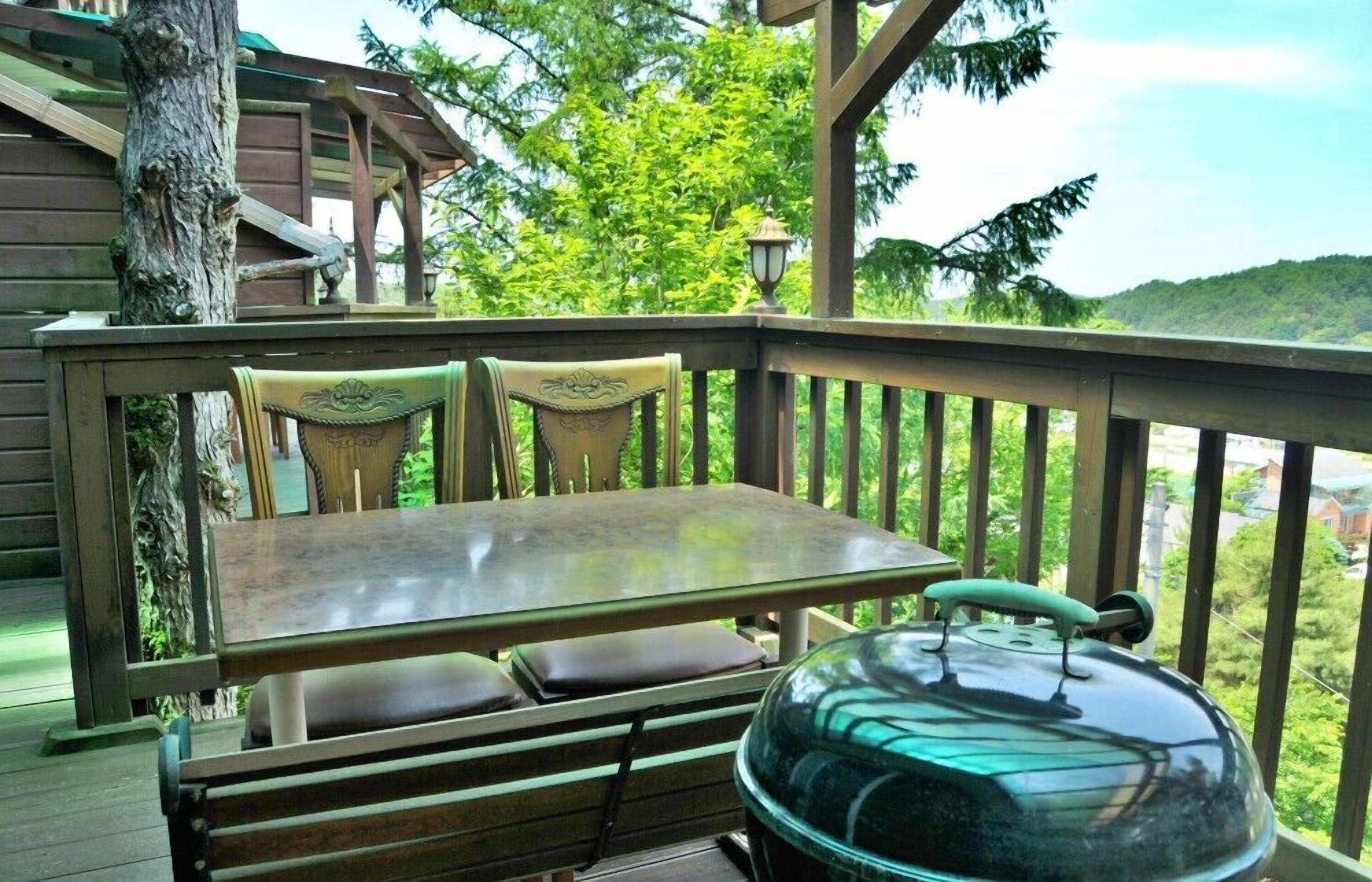 Una terraza de madera con una mesa y sillas, una parrilla y vistas a una ladera boscosa.