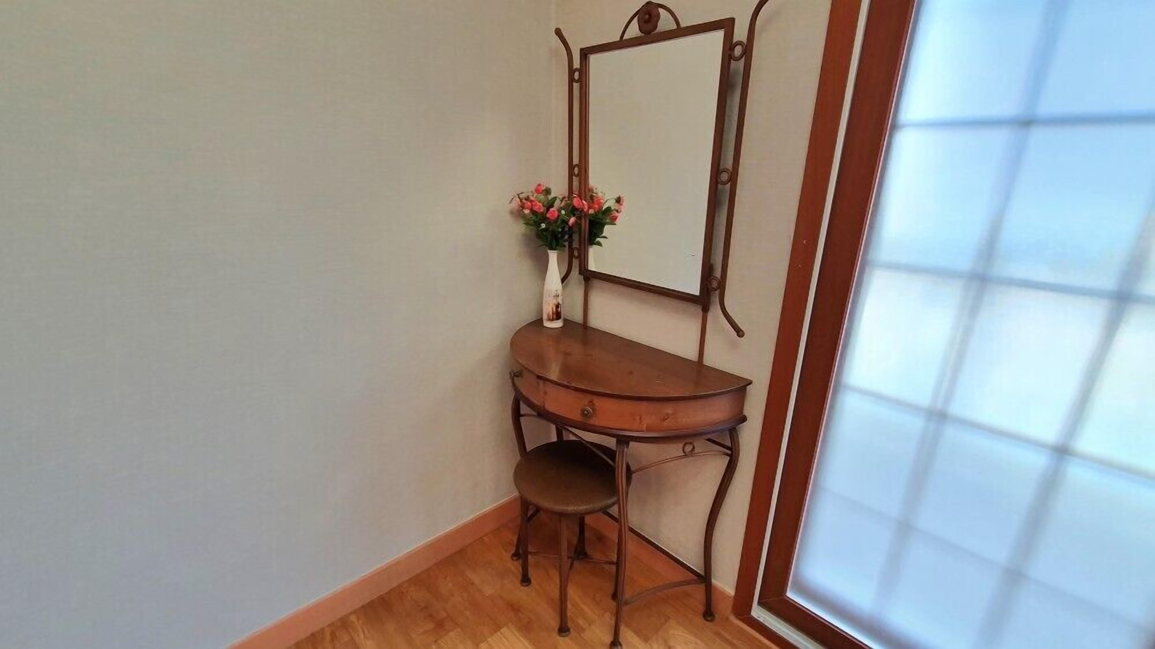 Habitación de esquina con tocador de madera, espejo y un taburete pequeño.