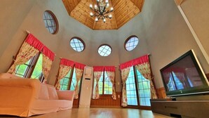 A spacious room with a high ceiling, wooden paneling, a chandelier, a television, and a sofa. - Castel on the hill pension (Hoengseong)