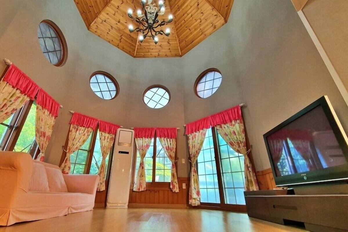 Ein geräumiger Raum mit hoher Decke, Holzwandverkleidung, einem Kronleuchter, einem Fernseher und einem Sofa.
