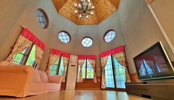 A spacious room with a high ceiling, wooden paneling, a chandelier, a television, and a sofa.