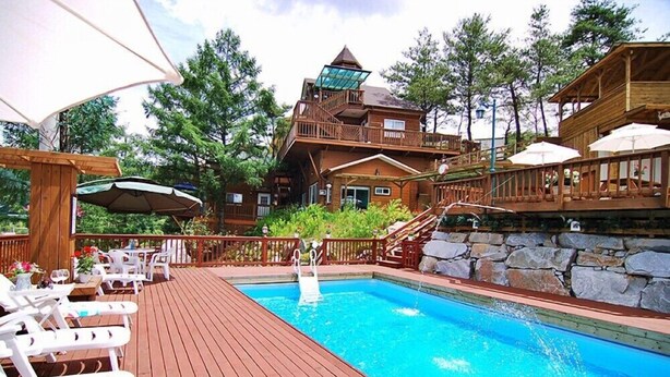 A wooden deck with a swimming pool, outdoor seating, and a stone wall. - Castel on the hill pension (Hoengseong)