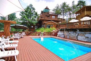 A wooden deck with a swimming pool, outdoor seating, and a stone wall. - Castel on the hill pension (Hoengseong)
