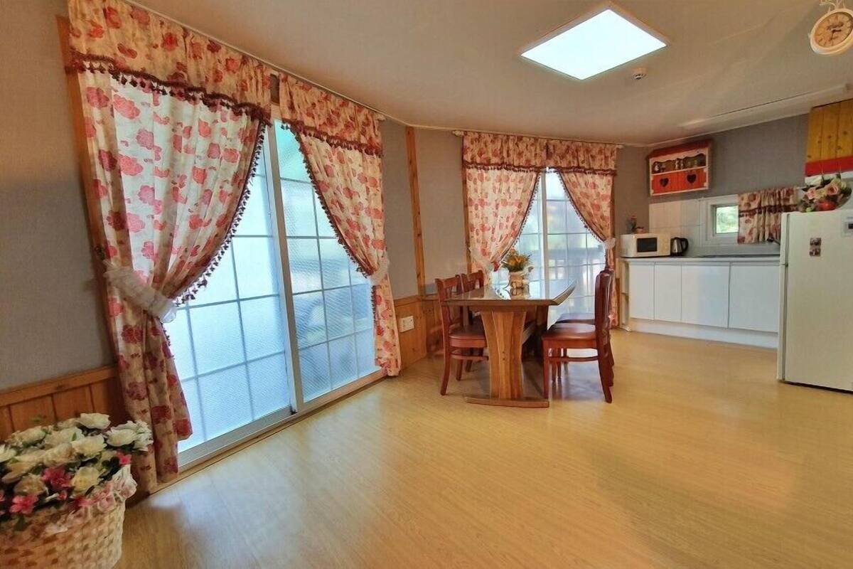 Ein gemütliches Zimmer mit einem Holzesstisch, Stühlen und einem Fenster mit blumigen Vorhängen.