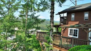 A wooden cabin with a balcony, surrounded by tall trees and a mountainous landscape. - Castel on the hill pension (Hoengseong)