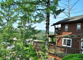 A wooden cabin with a balcony, surrounded by tall trees and a mountainous landscape.