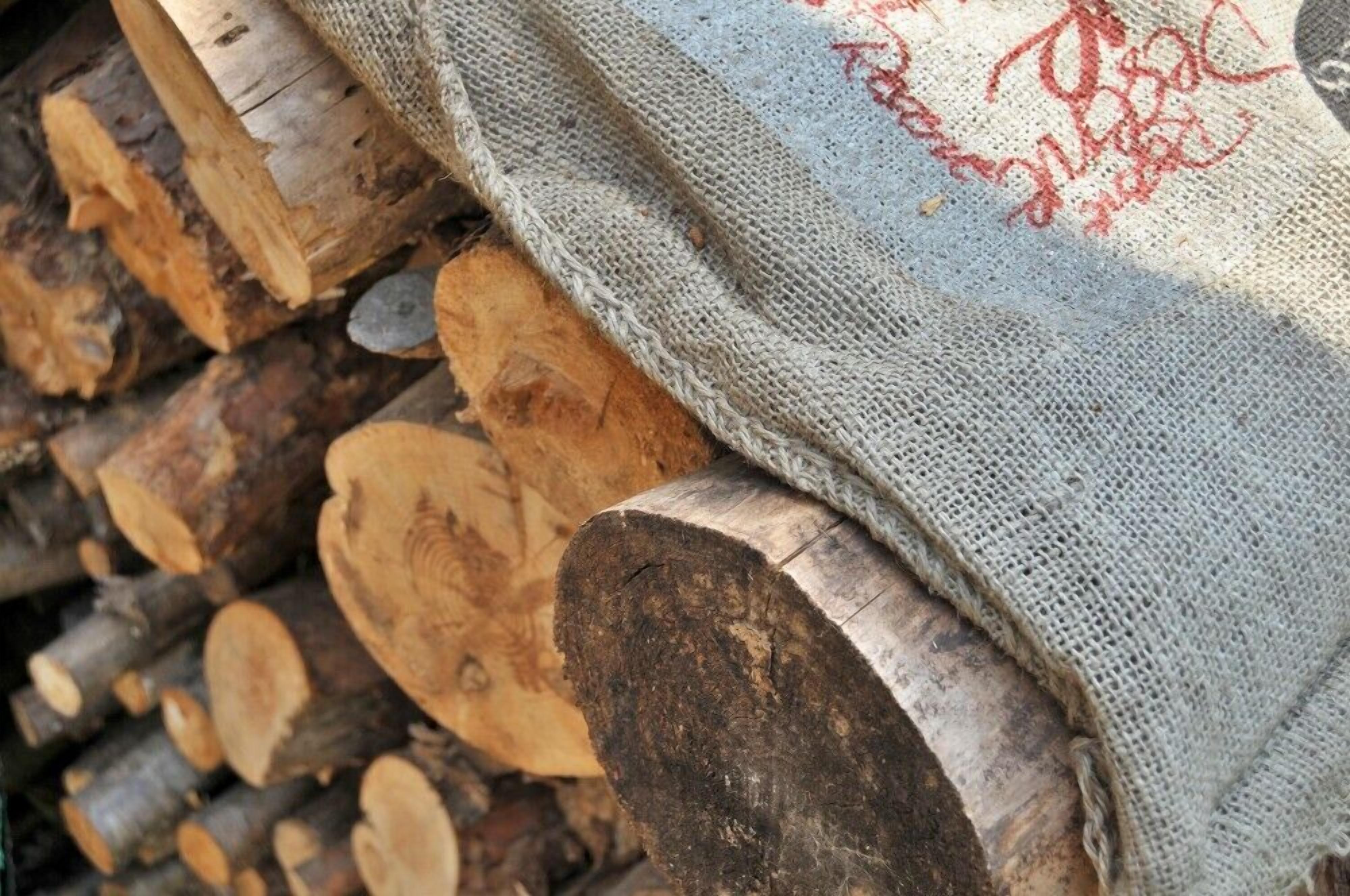 Una bossa de jute amb text vermell que cobreix parcialment un munt de llogs tallats.