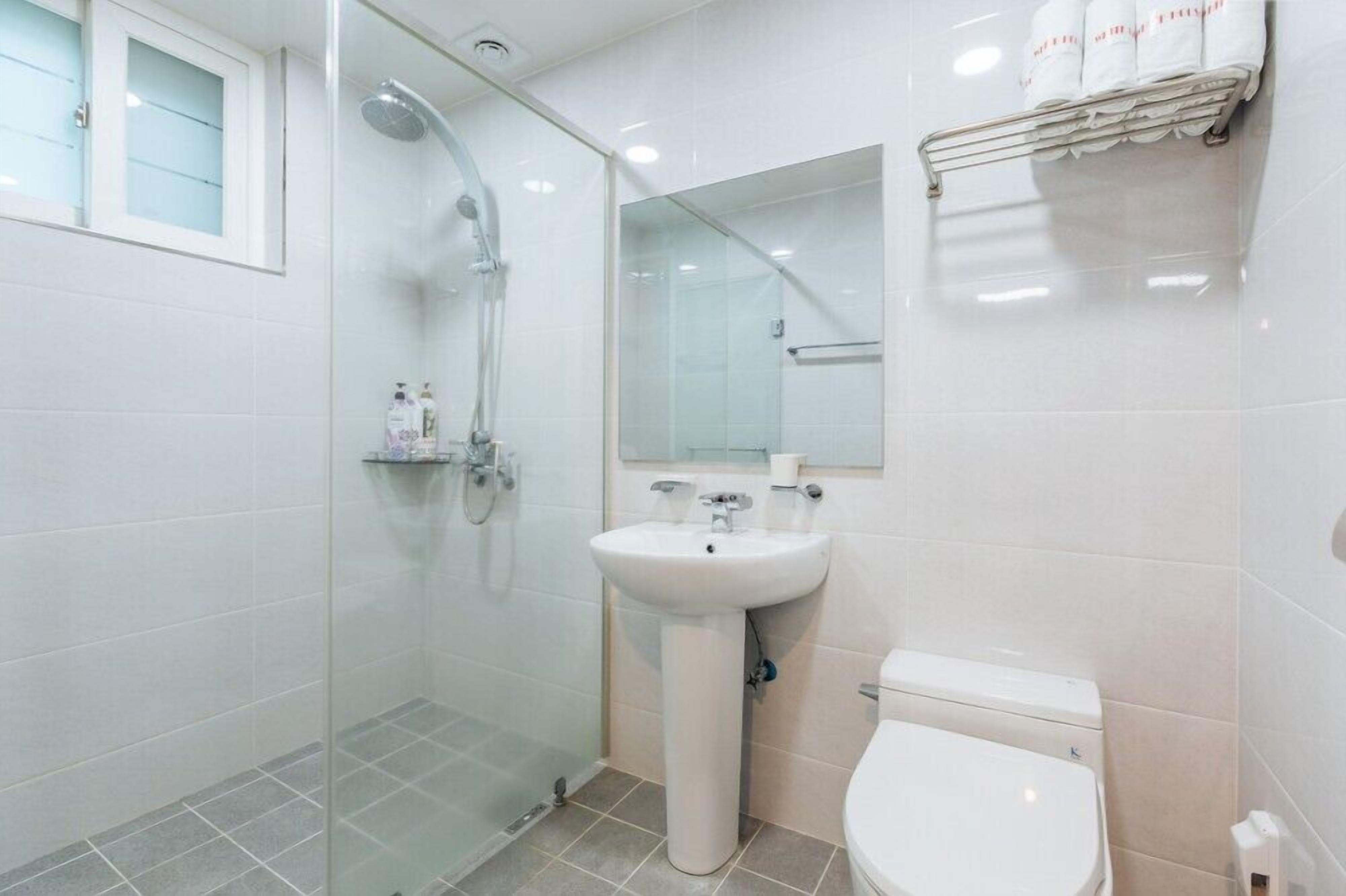 Un baño moderno con cabina de ducha de vidrio, lavamanos pedestal y un inodoro.