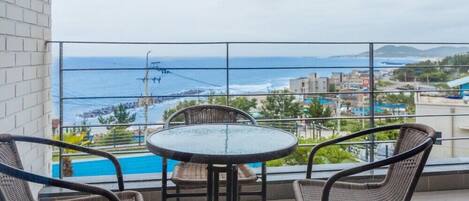 A balcony with a glass table and wicker chairs, overlooking a beach and cityscape.