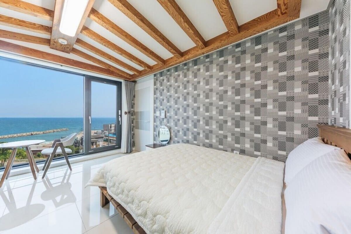 A bedroom with a large bed, a view of the sea, and a balcony with a table and chairs.