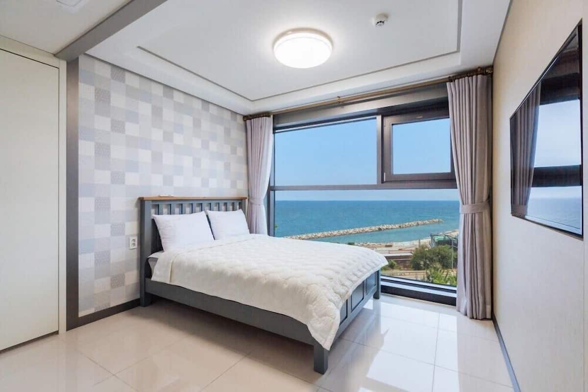 A bedroom with a bed, a large window with a view of the sea, and a checkered wall pattern.