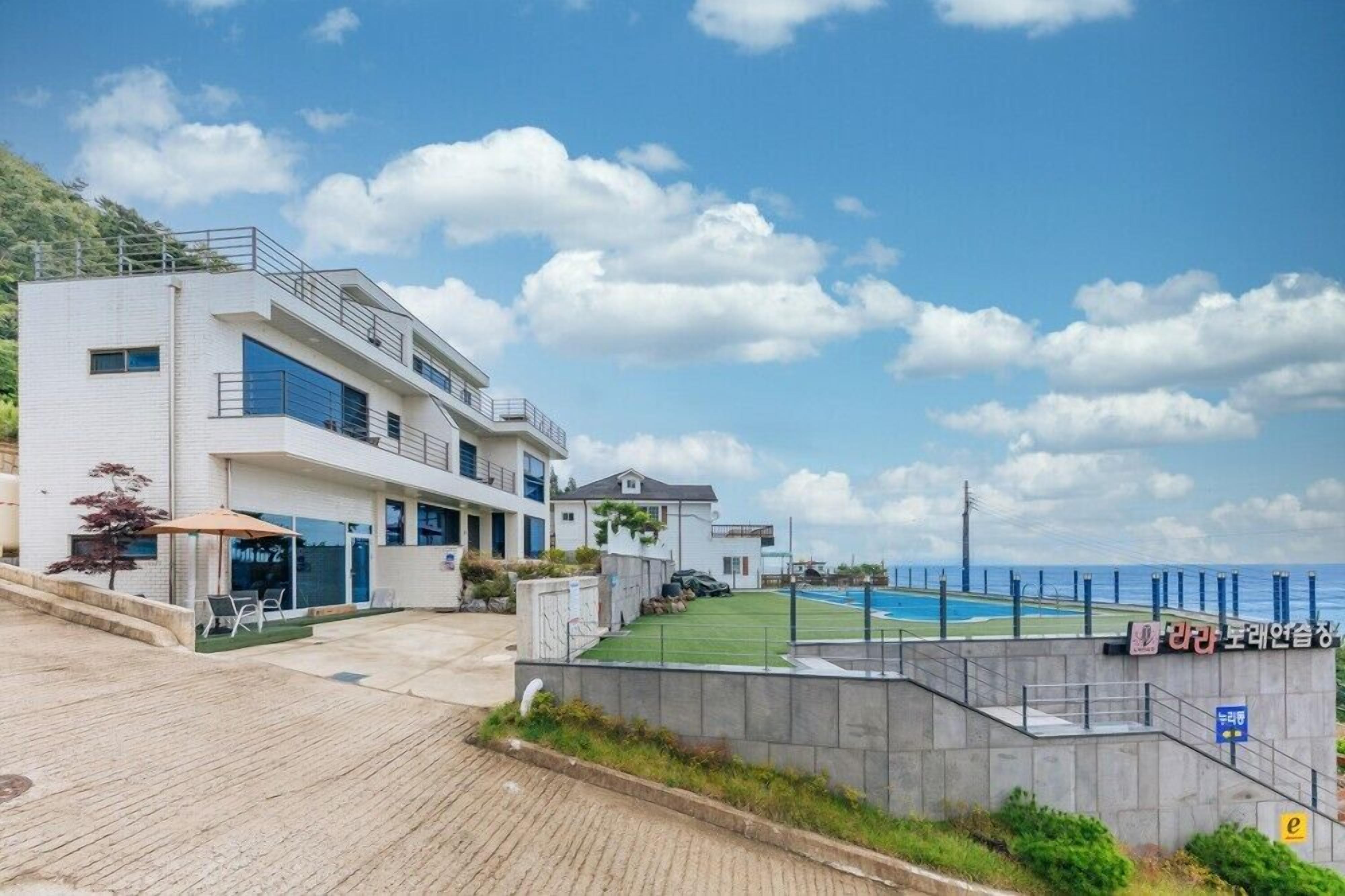 Una casa moderna de dos pisos con piscina, un patio con sillas y vista al mar.