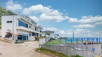 Una casa moderna de dos pisos con piscina, un patio con sillas y vista al mar.