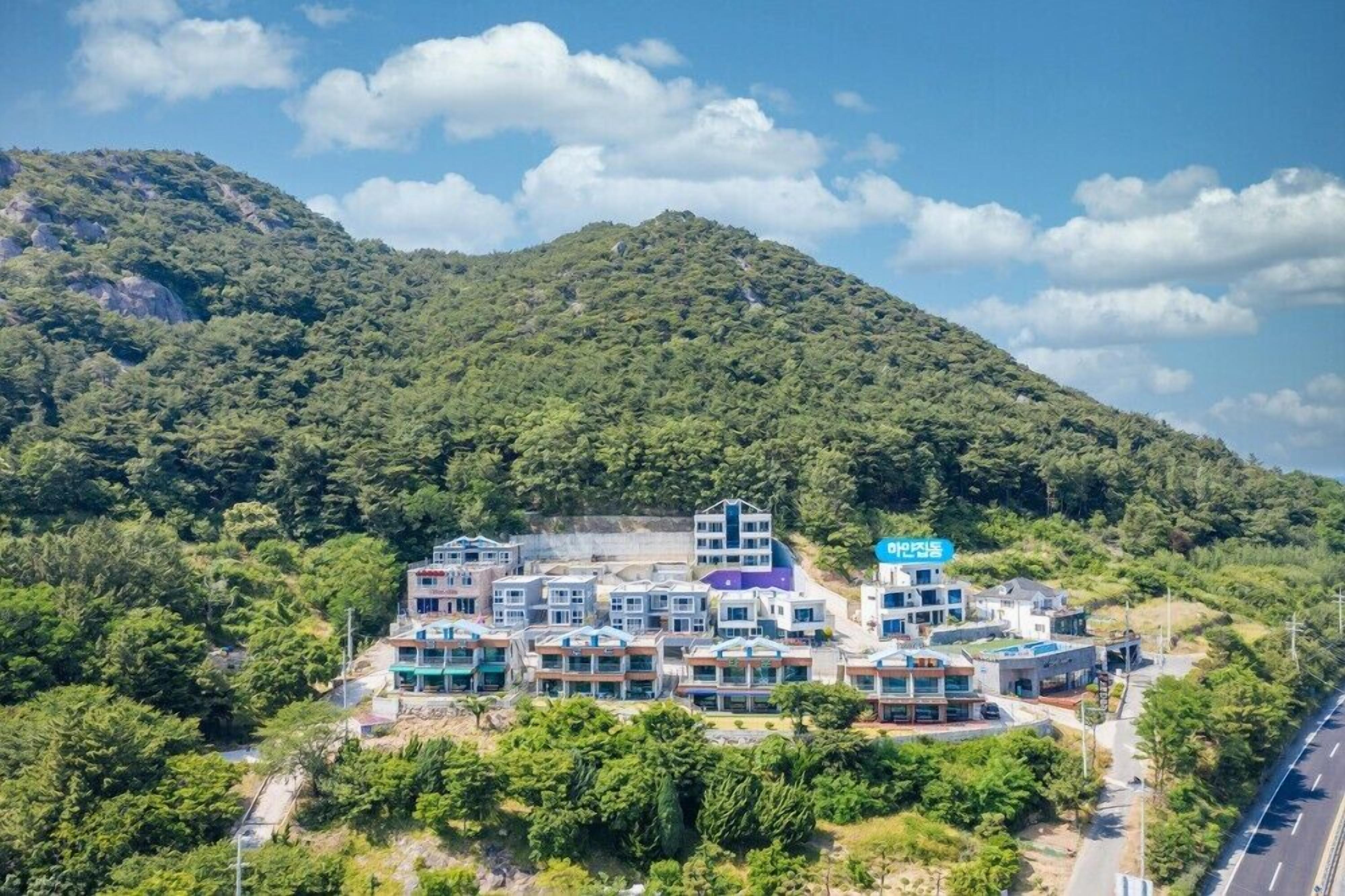 A modern hotel complex with multiple buildings, surrounded by lush greenery and a mountainous backdrop.