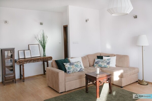 Ein Wohnzimmer mit einem beigen Sofa, einem Holztisch, einer Stehlampe und einem kleinen Beistelltisch mit einer Vase.