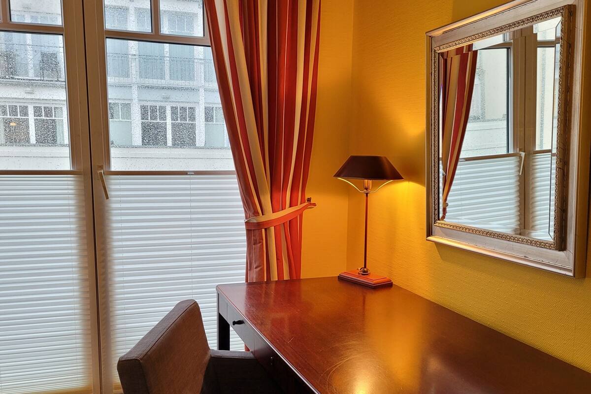 A hotel room with a wooden desk, a chair, a lamp, and a large mirror.